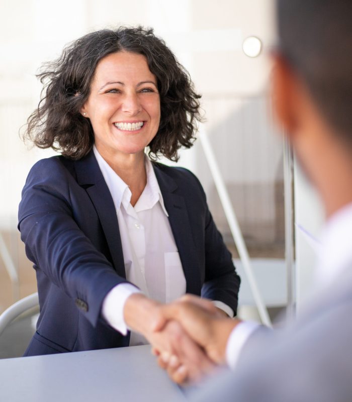 Happy successful business colleagues meeting outside and closing deal. Joyful business woman and man sitting at table, talking and shaking hands. Closing deal concept